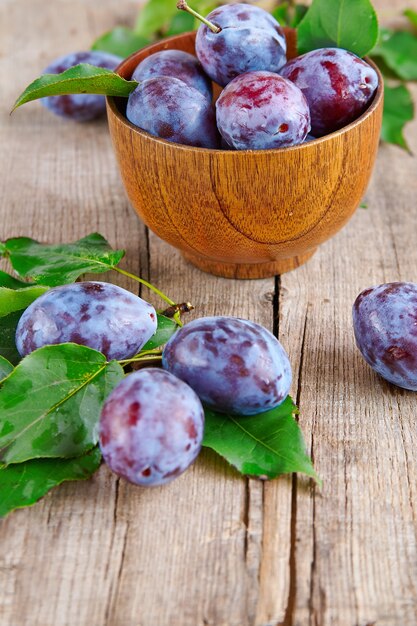 Fresh prunes in the wooden cup on a rustic wooden table.