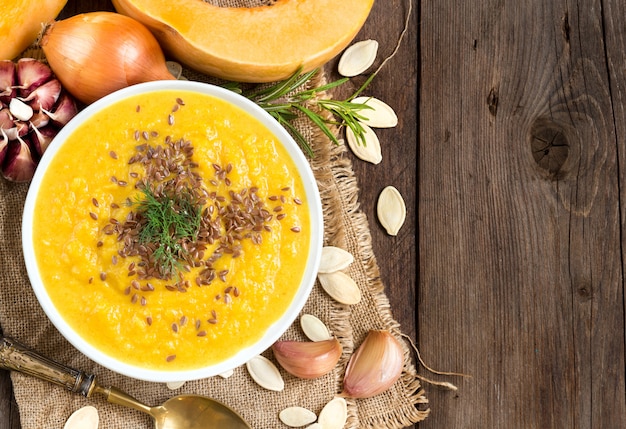 Fresh pumpkin soup puree and raw vegetables on a wooden table with copy space