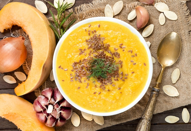 Fresh pumpkin soup puree and raw vegetables on a wooden table