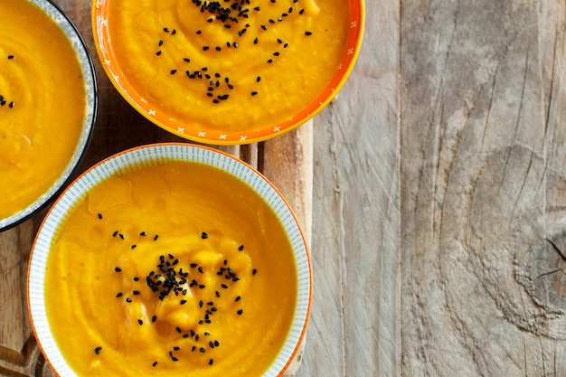 Fresh pumpkin soup in three bowls on a wooden table