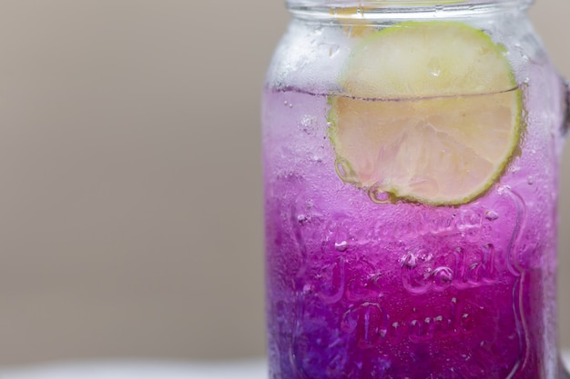 Foto pisello di farfalla porpora fresca o fiore del pisello blu e succo di limone in vetro con fondo verde della sfuocatura