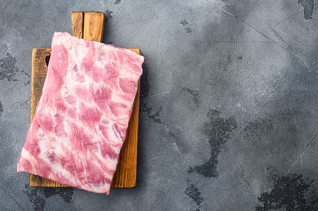 Fresh rack of raw pork spare ribs set, on wooden cutting board, on gray stone table, top view flat lay