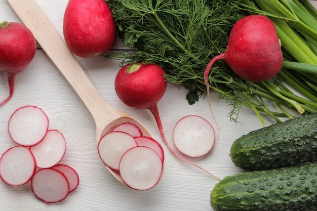 Fresh radish. Spring fresh vegetables radishes, cucumber, green onions and greens on a white wooden table. ingredients for cooking. top view