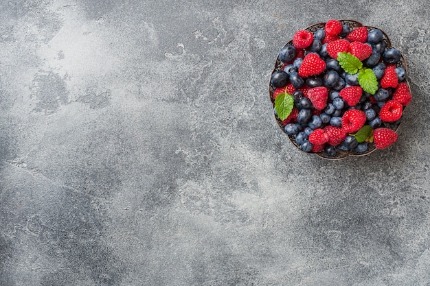 Fresh raspberries and blueberries in plate on dark surface