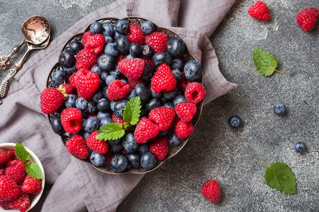 Fresh raspberries and blueberries in plate on dark surface