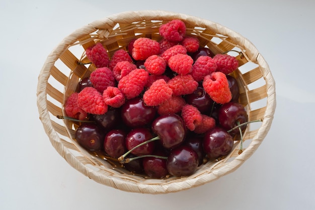 Fresh raspberries and cherries in a bucket on the white background