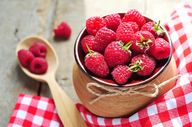 Fresh raspberries in clay pot on wooden background