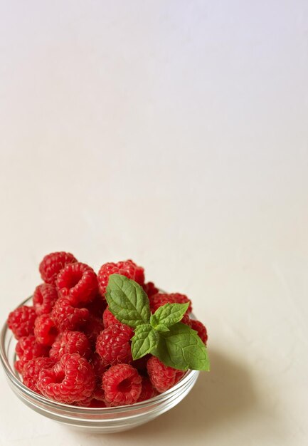 Photo fresh raspberries in the clear glass bowl on the white background with copyspace