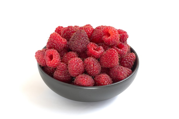 Fresh raspberries in dark bowl isolated on white background.