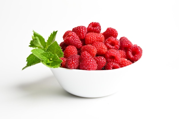 Fresh raspberries and mint leaves in white bowl isolated on white background Close up