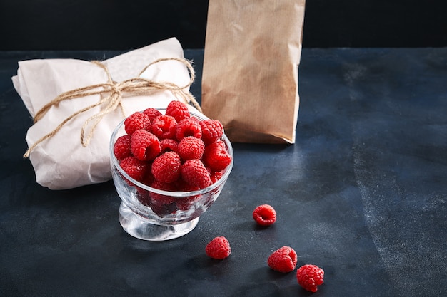 Fresh raspberries in a plate on a blue background. Food delivery concept, eco-friendly packaging