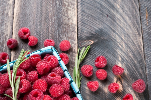 Fresh raspberries and rosemary in a basket on a wooden table