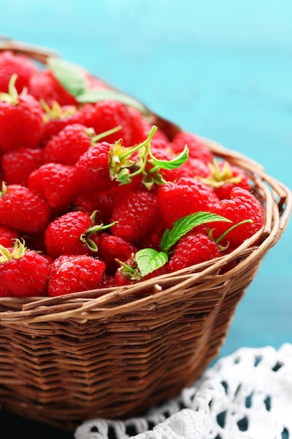 Fresh raspberries in wicker basket on wooden table closeup