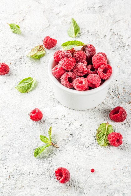 Fresh raspberries with mint in small bowl, on grey stone background, copy space