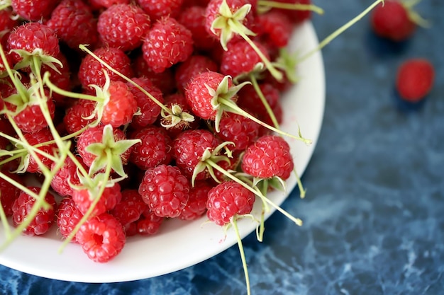 Fresh raspberries with tails on a white plate Closeup