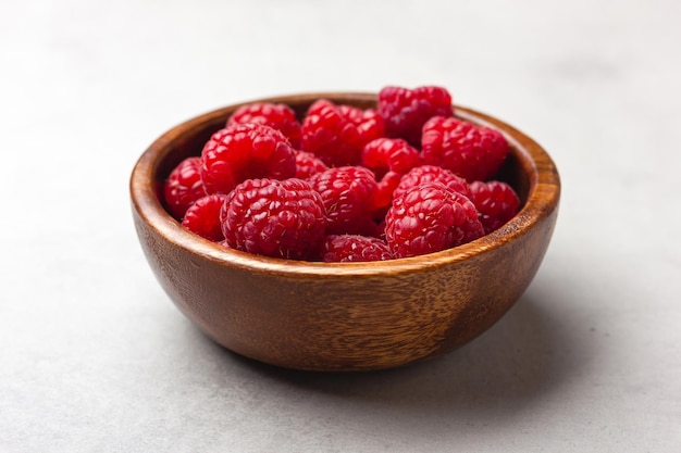 Fresh raspberries in a wooden bowl on a light grey background Red berries