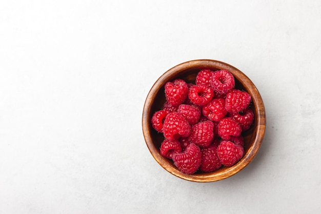 Fresh raspberries in a wooden bowl on a light grey background