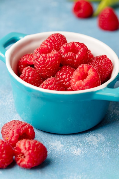 Fresh raspberry fruits in blue bowl blue background