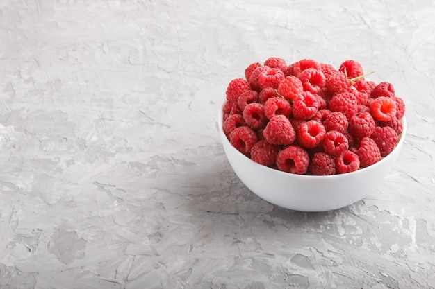 Fresh raspberry in white bowl on gray concrete background. side view.