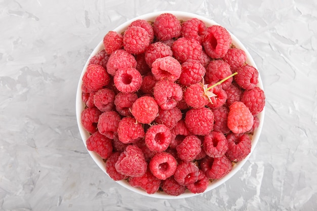 Fresh raspberry in white bowl on gray concrete background. top view.