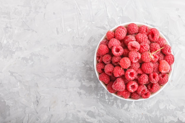 Fresh raspberry in white bowl on gray concrete background