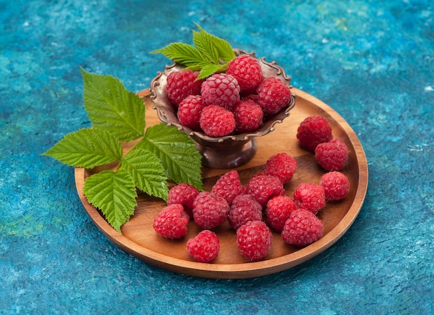 Fresh raspberry in a wooden plate on a blue background