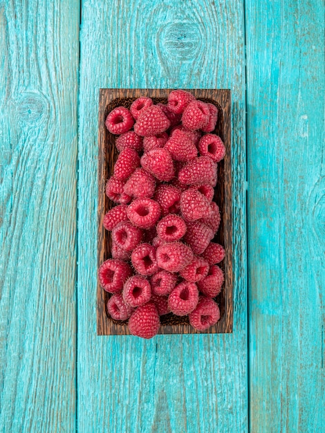 Fresh raspberry in a wooden plate on blue