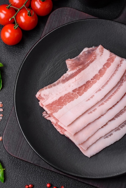 Photo fresh raw bacon cut into slices with salt spices and herbs on a dark textured concrete background