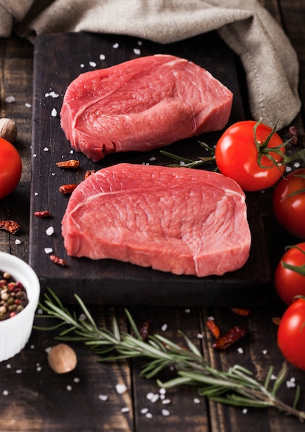 Fresh raw beef steak meat on wooden kitchen board with tomatoes and pepper