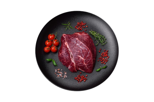 Fresh raw beef steak with salt spices and herbs on a dark concrete background