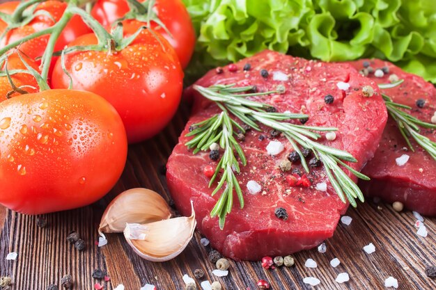 Fresh raw beef steak with spice and vegetable on brown wooden table