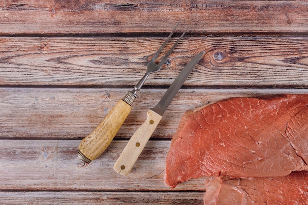 Fresh raw beef steaks with knife on wooden table