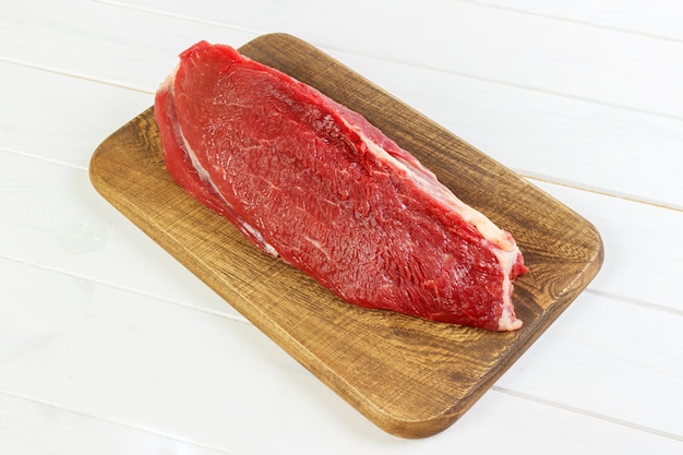 Fresh raw beef on a wooden cutting board on dark 