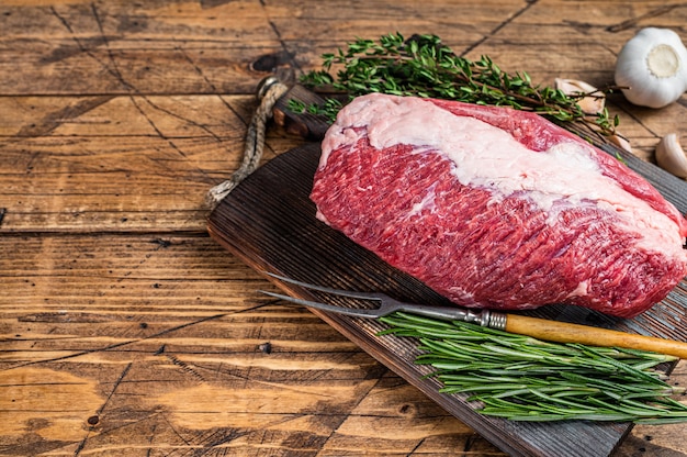 Fresh Raw brisket beef meat prime cut on a wooden  board with herbs