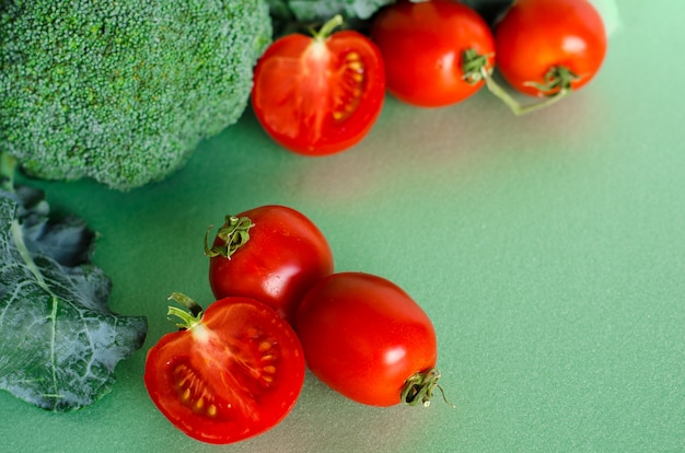 Свежие сырцовые брокколи и томаты на зеленой предпосылке и linen ткани. органическая еда.