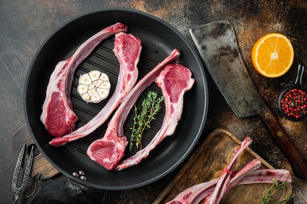 Fresh raw butchers lamb beef cutlets, with ingredients carrot orange, herbs, on frying cast iron pan, on old dark rustic table, top view flat lay