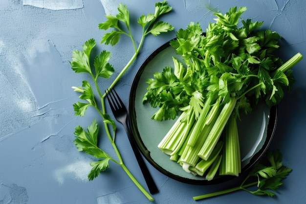 Fresh raw celery stalks with leaves arranged on a dark plate against a textured blue background