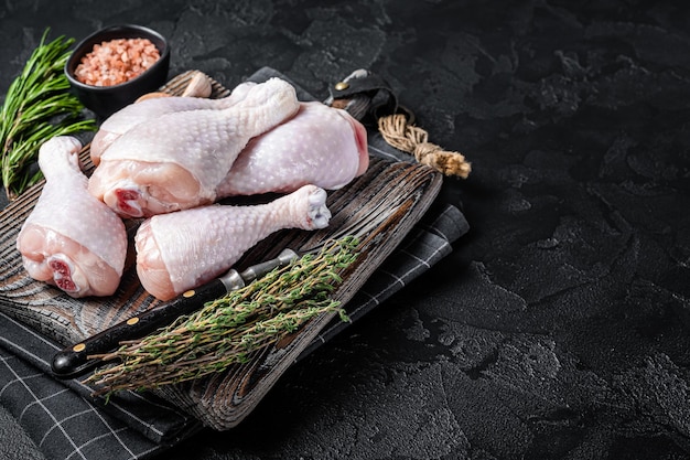 Fresh Raw chicken drumsticks legs on wooden cutting board. Black background. Top view. Copy space.