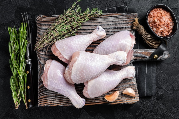 Gambe di cosce di pollo crudo fresco su tagliere di legno sfondo nero vista dall'alto