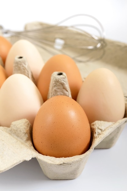 Uova crude fresche del pollo in contenitore di cartone, su fondo bianco. primo piano sulle uova marroni e bianche.