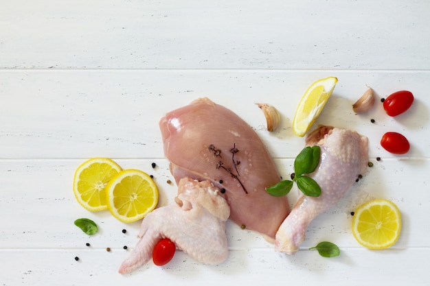 Fresh raw chicken fillets, wing, thigh and lower leg with a lemon, spices and basil on the kitchen table. Copy space. Top view.