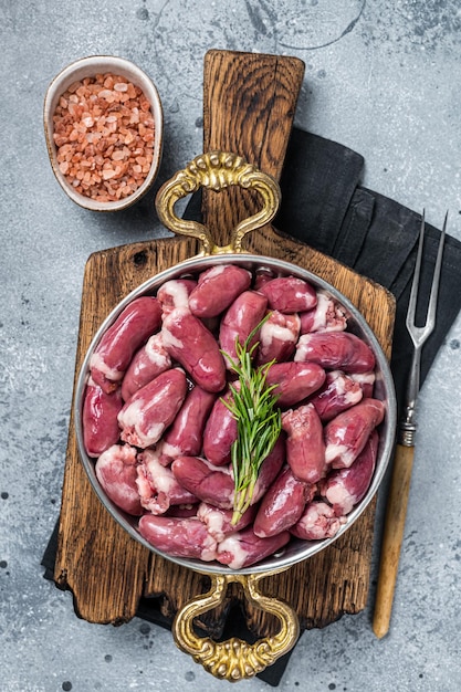 Cuori di pollo crudo fresco in una padella con erbe sfondo grigio vista dall'alto