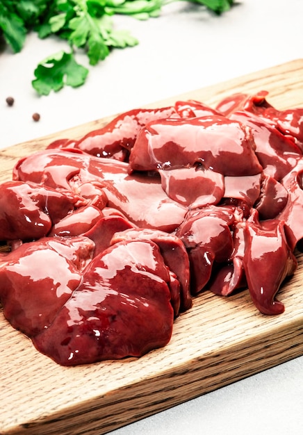 Fresh raw chicken liver on cutting board and ingredients for\
cooking on concrete white stone kitchen table top view copy\
space