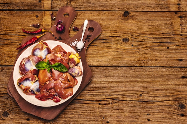 Frattaglie di pollo crudo fresco: cuore, fegato, stomaco con spezie secche, sale marino, peperoncino sul tavolo di legno