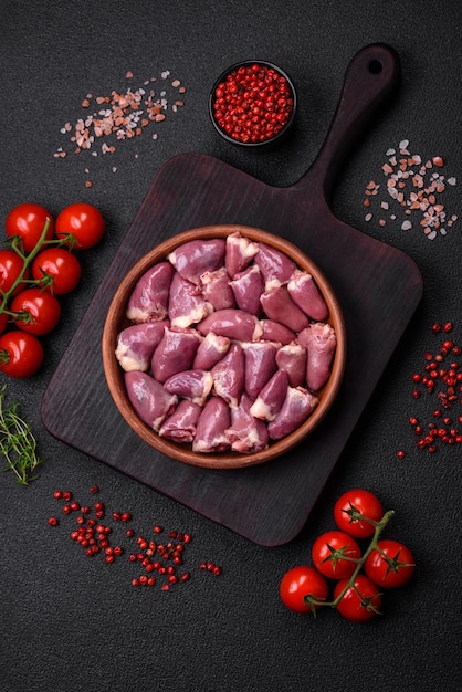 Fresh raw chicken or turkey hearts in a ceramic plate with salt spices and herbs on a dark concrete background