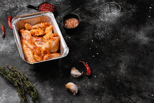 Свежие сырые куриные крылышки и ингредиенты для соуса барбекю, на черном фоне темного каменного стола, с местом для текста