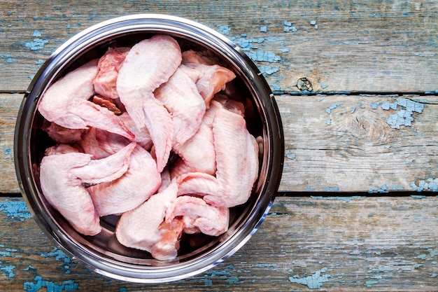 Fresh raw chicken wings in a steel bowl on a rustic table