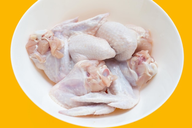 Fresh raw chicken wings in white bowl on yellow background.