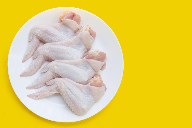 Fresh raw chicken wings in white bowl on yellow background