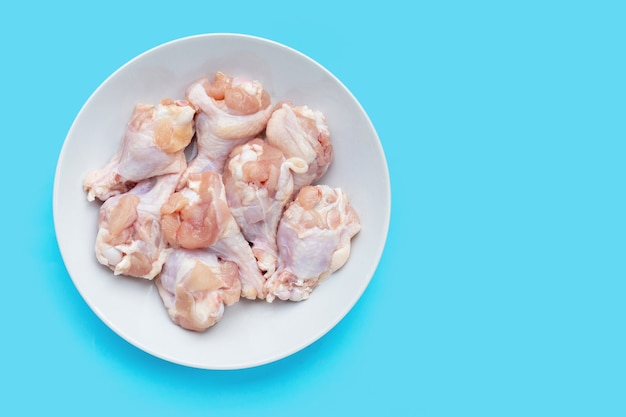 Fresh raw chicken wings (wingstick) in white plate on blue background.